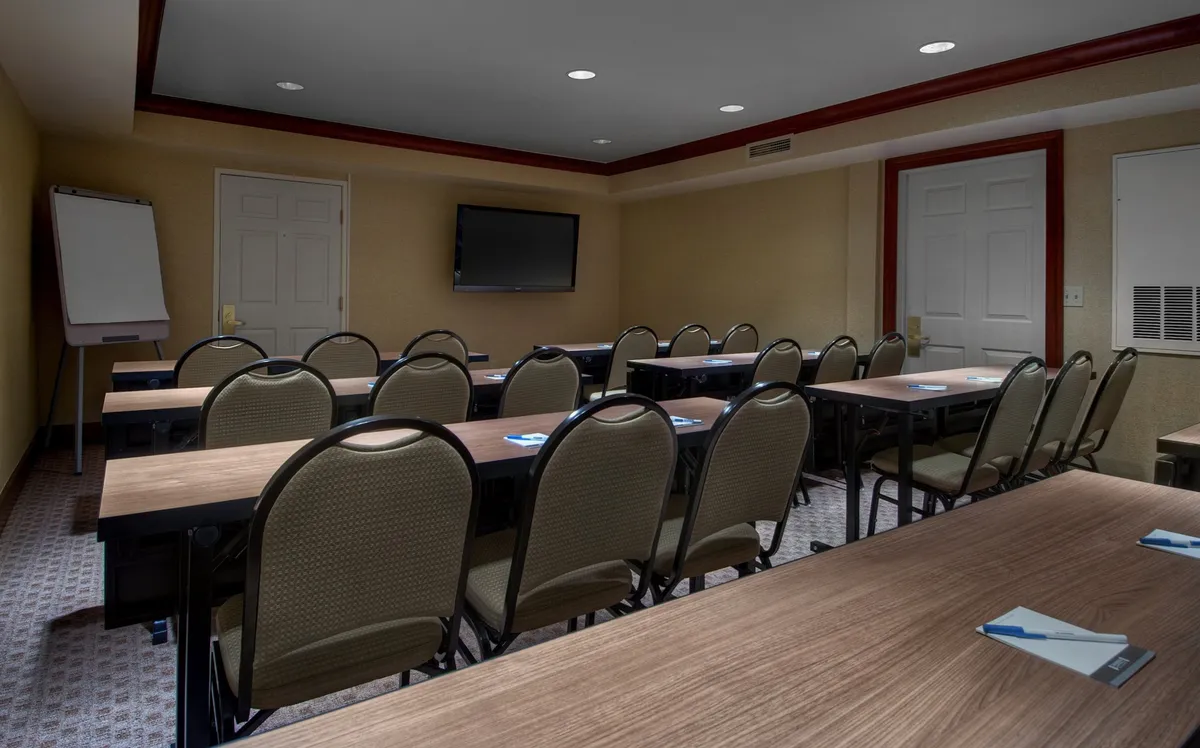 A dedicated business center setup with rows of tables, chairs, a presentation screen, and a whiteboard. The environment is arranged for productivity and collaboration—ideal for business meetings, solo work, or small group sessions.
