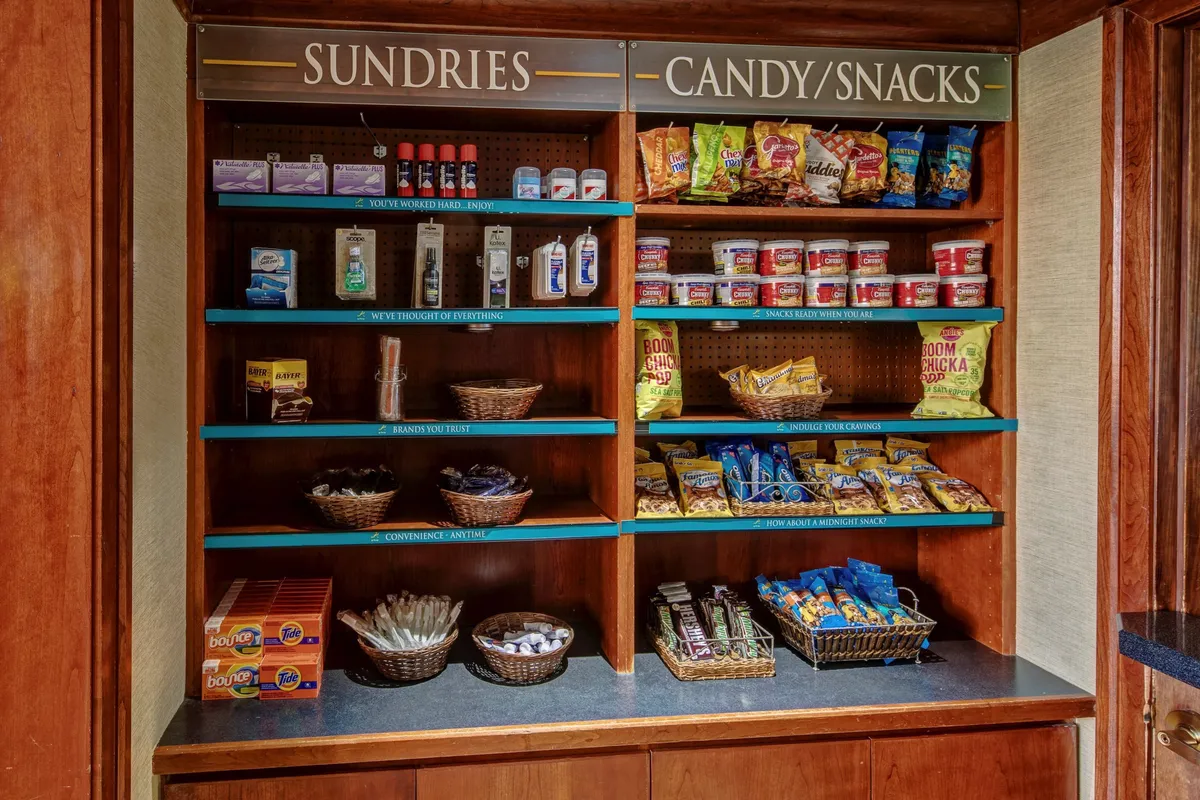 A well-stocked sundries shelf lines one wall, with baskets of snacks and a variety of convenient items. The scene exudes a casual, accessible atmosphere, ideal for guests grabbing a quick bite or picking up essentials for meal preparation.